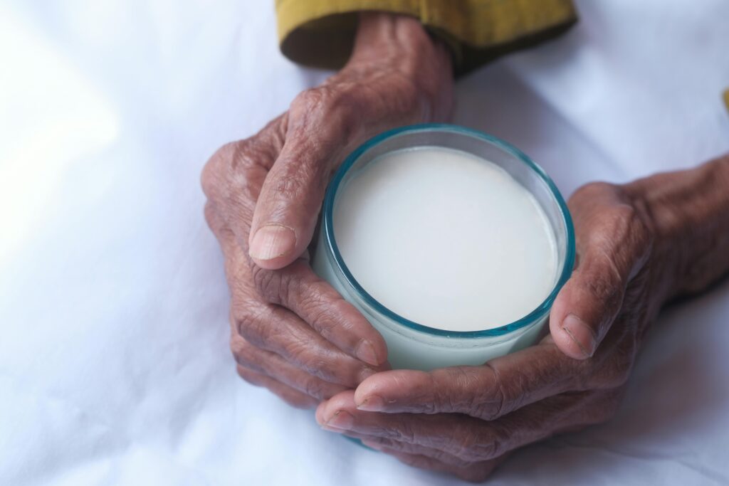 Close-up of elderly hands holding a glass of milk, symbolizing care and nourishment.
