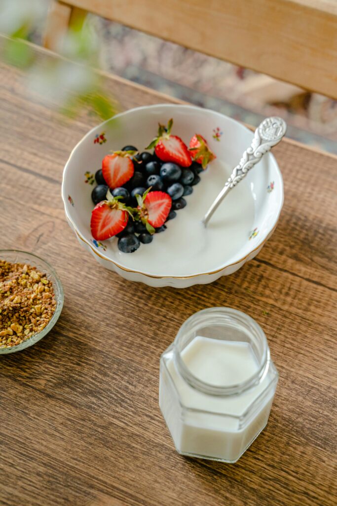 Top view of a breakfast bowl with strawberries, blueberries, yogurt, and milk on a wooden table.