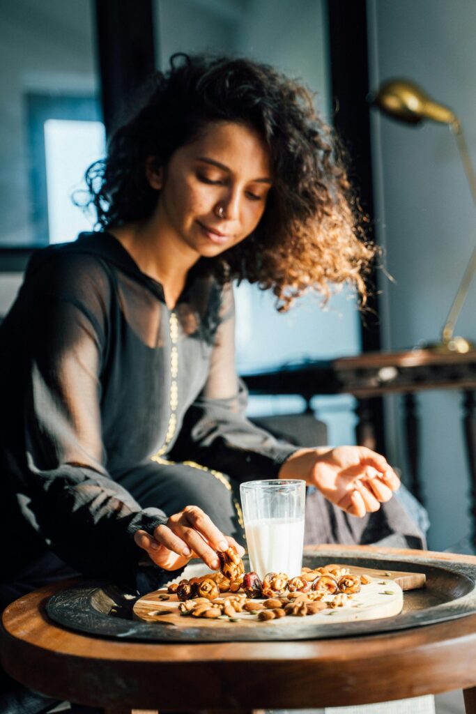 Woman reaching for nuts and dates with a glass of milk, enjoying a healthy snack.